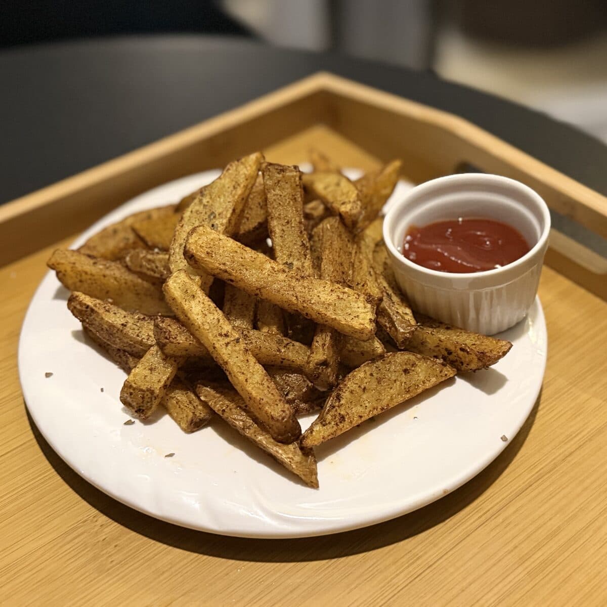 A plate of seasoned fries with a dip, on a wooden tray